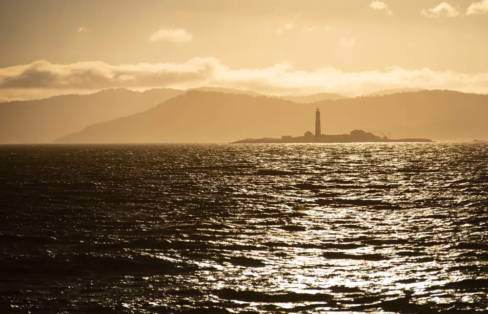 Lighthouse island silhouetted in golden haze across the water