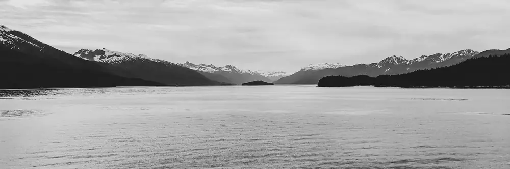 Mountains across a still bay, black and white panorama