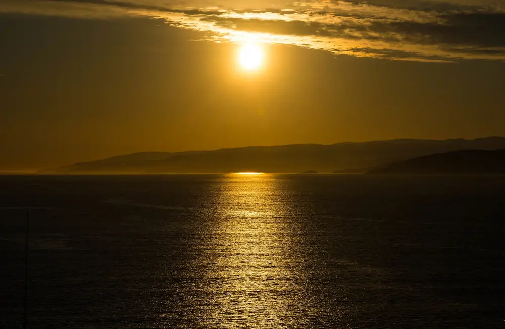 Golden sun breaking through cloud over open water