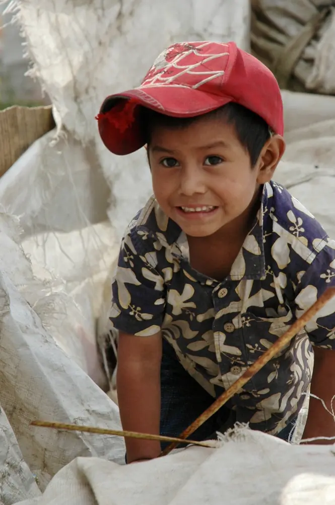 Boy in a red cap holding a stick, seated on sacking