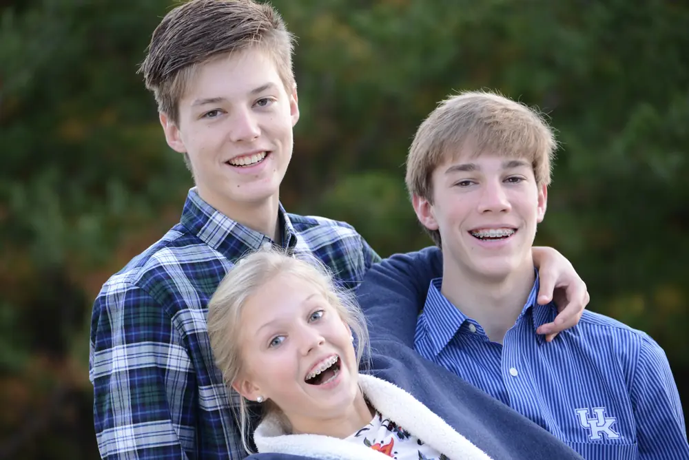 Three siblings laughing together outdoors in autumn