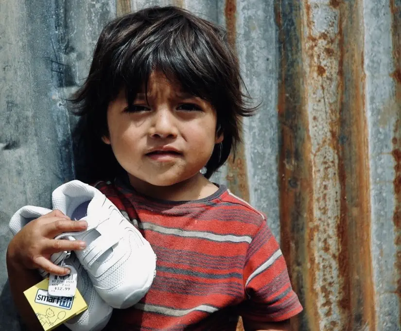 Boy holding a new pair of shoes against a rusted wall