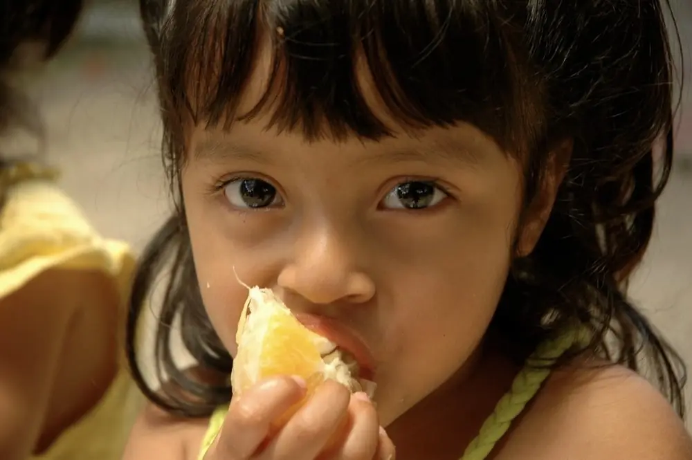 Girl eating a piece of an orange, close up